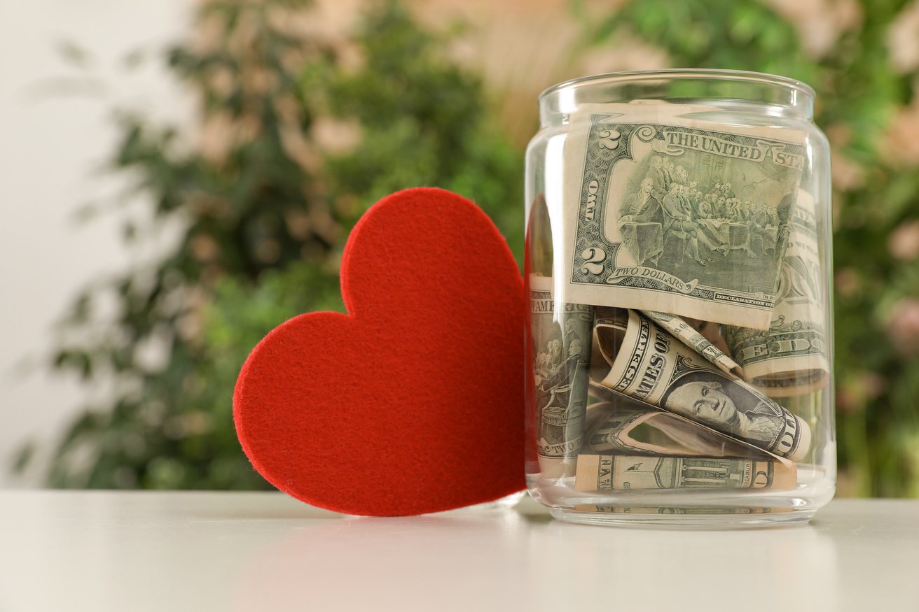 Red Heart and Donation Jar with Money on Table against Blurred Background